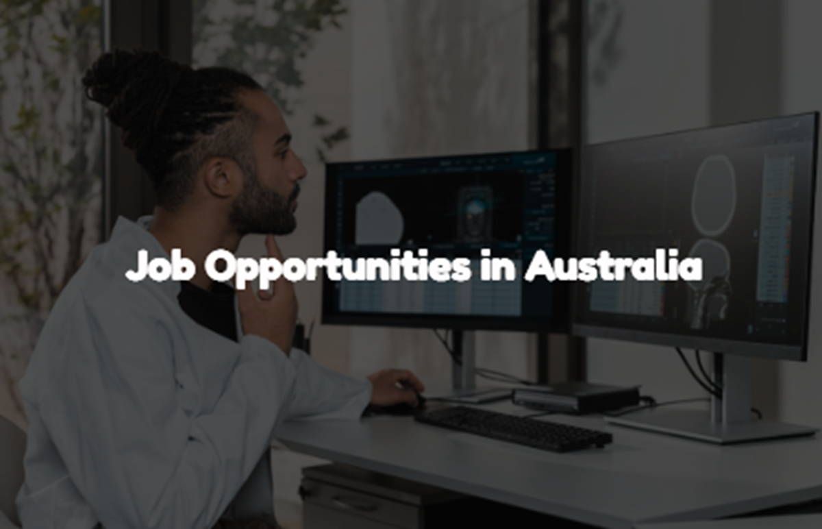 A man in a white shirt working on a computer with a message about job opportunities in Australia shown on the screen